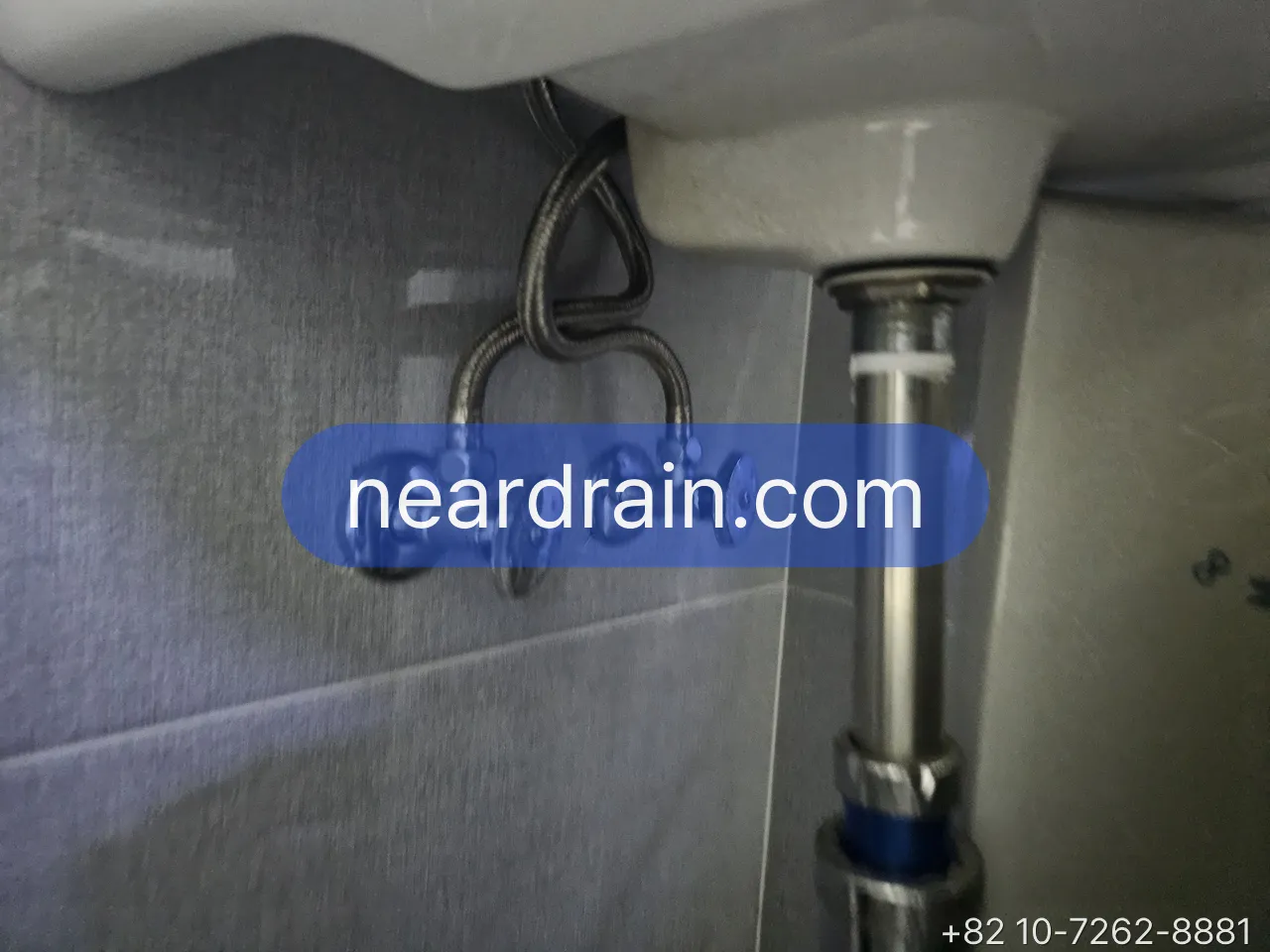 Two chrome angle valves on a tiled wall under a basin, braided hoses rising to the tap