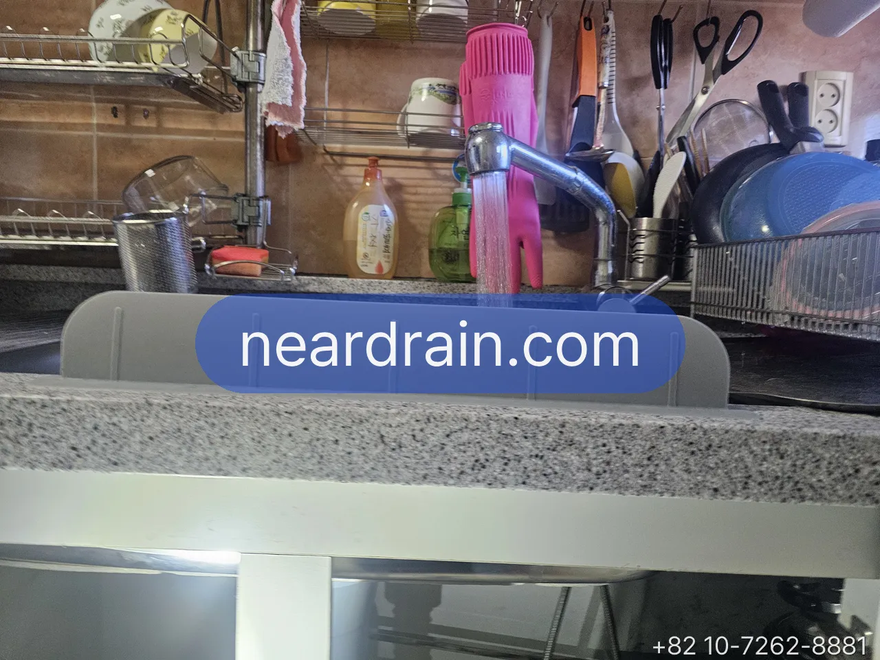 Kitchen mixer tap running a thin stream of water into a stainless sink, dish rack and utensils behind